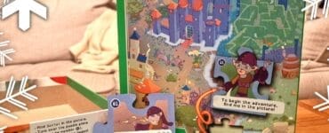 Colorful jigsaw puzzle box titled "My Puzzle Adventure: Dragon," featuring an illustrated map with a castle, characters, and interactive puzzle pieces. The image showcases the puzzle's storytelling aspect, with text prompts and a whimsical design suitable for children. Snowflakes are subtly placed around the image, adding a festive touch.