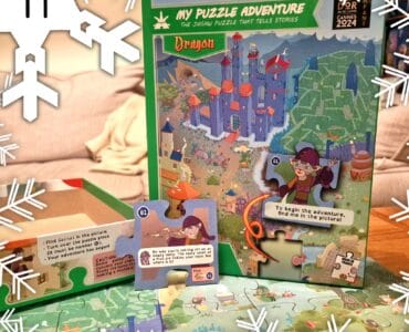 Colorful jigsaw puzzle box titled "My Puzzle Adventure: Dragon," featuring an illustrated map with a castle, characters, and interactive puzzle pieces. The image showcases the puzzle's storytelling aspect, with text prompts and a whimsical design suitable for children. Snowflakes are subtly placed around the image, adding a festive touch.