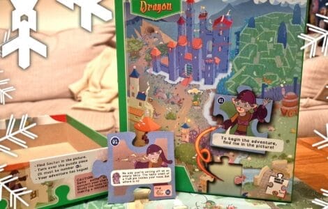 Colorful jigsaw puzzle box titled "My Puzzle Adventure: Dragon," featuring an illustrated map with a castle, characters, and interactive puzzle pieces. The image showcases the puzzle's storytelling aspect, with text prompts and a whimsical design suitable for children. Snowflakes are subtly placed around the image, adding a festive touch.