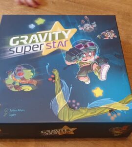 Colorful board game box for "Gravity Super Star" featuring playful characters and vibrant artwork, designed by Julian Allain and Gyom. The box showcases a dynamic theme with elements of gravity and adventure, ideal for family game nights.