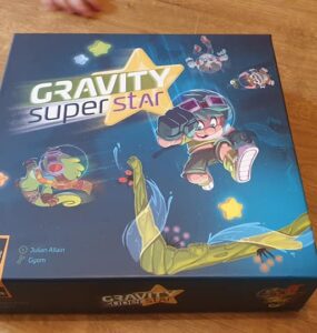 Colorful board game box for "Gravity Super Star" featuring playful characters and vibrant artwork, designed by Julian Allain and Gyom. The box showcases a dynamic theme with elements of gravity and adventure, ideal for family game nights.