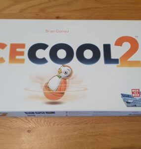 Ice Cool 2 board game box featuring colorful graphics and a penguin character, designed by Brian Gomez, displayed on a wooden table.