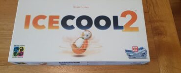 Ice Cool 2 board game box featuring colorful graphics and a penguin character, designed by Brian Gomez, displayed on a wooden table.