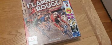 Flamme Rouge board game box featuring a vintage cycling theme, with vibrant artwork of cyclists racing. The box displays multiple awards, including the 2018 As d'Or and Mensa Select, highlighting its popularity and acclaim. The game is designed for family and strategy enthusiasts.