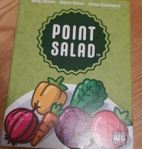 Board game "Point Salad" featuring colorful vegetable illustrations on the box cover, designed by Molly Johnson, Robert Melvin, and Shawn Stankiewich. The artwork includes various vegetables like carrots, peppers, and leafy greens, set against a green background.