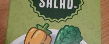 Board game "Point Salad" featuring colorful vegetable illustrations on the box cover, designed by Molly Johnson, Robert Melvin, and Shawn Stankiewich. The artwork includes various vegetables like carrots, peppers, and leafy greens, set against a green background.
