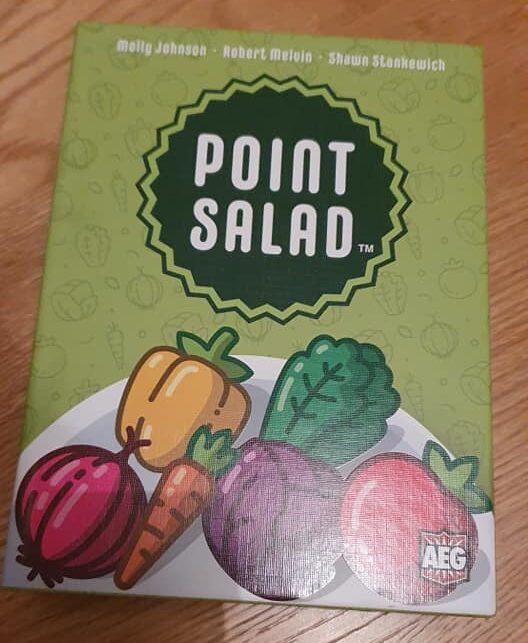 Board game "Point Salad" featuring colorful vegetable illustrations on the box cover, designed by Molly Johnson, Robert Melvin, and Shawn Stankiewich. The artwork includes various vegetables like carrots, peppers, and leafy greens, set against a green background.