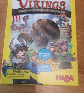 Colorful board game box for "Valley of the Vikings" by HABA, featuring Viking characters and barrels. The design highlights the game's theme of knocking over barrels while trying to stay dry. It includes a warning about choking hazards and mentions the game is suitable for ages 6 and up. Recognized as the Children's Game of the Year 2019.