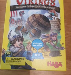 Colorful board game box for "Valley of the Vikings" by HABA, featuring Viking characters and barrels. The design highlights the game's theme of knocking over barrels while trying to stay dry. It includes a warning about choking hazards and mentions the game is suitable for ages 6 and up. Recognized as the Children's Game of the Year 2019.