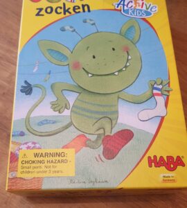 Colorful box of the children's game "Socken zocken" by HABA, featuring a cheerful green creature holding a sock, with a warning label about choking hazards.