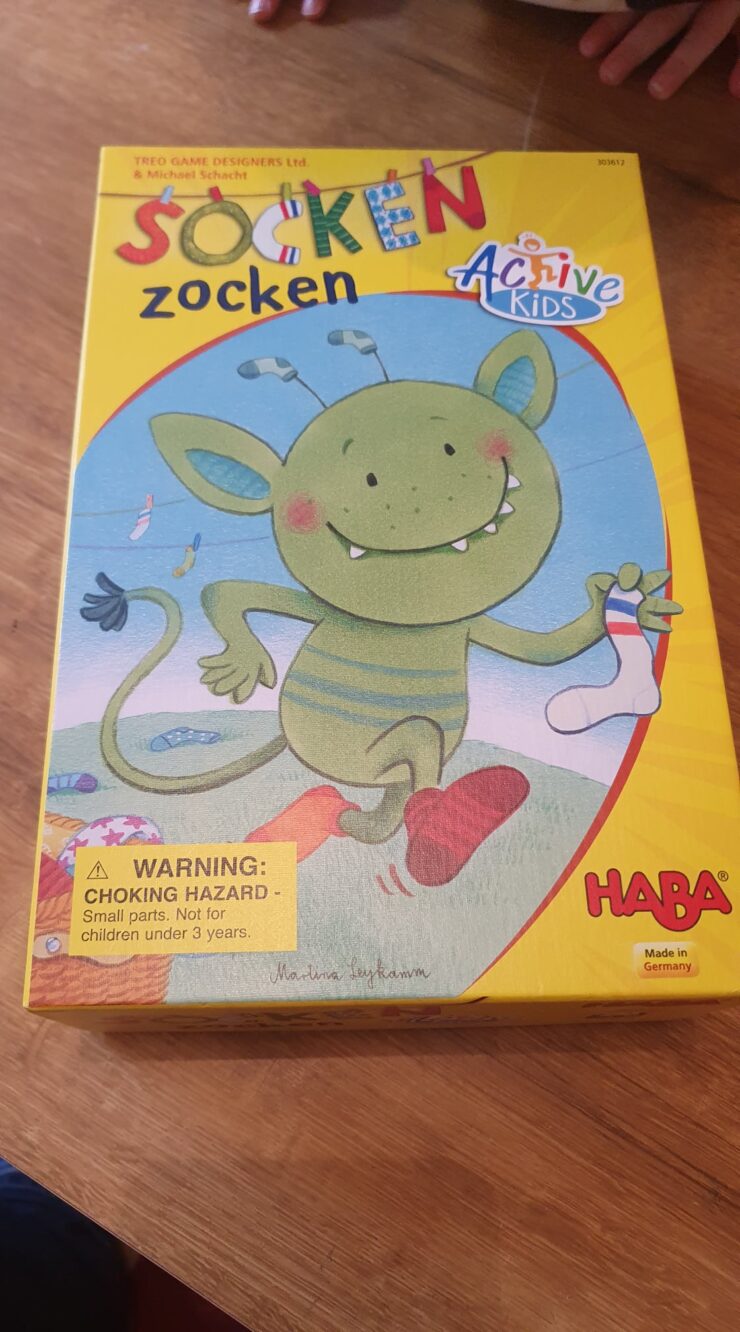 Colorful box of the children's game "Socken zocken" by HABA, featuring a cheerful green creature holding a sock, with a warning label about choking hazards.