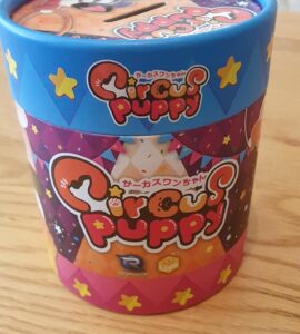 Colorful packaging of the "Circus Puppy" toy, featuring vibrant designs with stars and playful graphics, sitting on a wooden table.