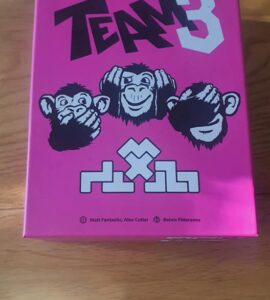 Colorful game box for "Team 3," featuring three cartoon monkeys with playful expressions, set against a bright pink background. The design includes the game's title and logos of the creators, Matt Fantastic, Alex Cutler, and Reinis Pētersons. Perfect for board game enthusiasts.