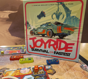 Board game "Joyride: Survival of the Fastest" featuring vibrant artwork of a futuristic car and game components displayed on a tabletop with a desert background. The game includes colorful vehicle tokens and strategic elements for players to engage in high-speed challenges.