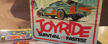 Board game "Joyride: Survival of the Fastest" featuring vibrant artwork of a futuristic car and game components displayed on a tabletop with a desert background. The game includes colorful vehicle tokens and strategic elements for players to engage in high-speed challenges.