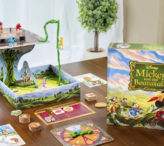 Colorful Disney board game "Mickey and the Beanstalk" displayed on a wooden table, featuring a 3D game board, character pieces, and game cards, set in a bright indoor environment with a plant in the background.