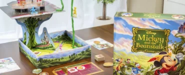 Colorful Disney board game "Mickey and the Beanstalk" displayed on a wooden table, featuring a 3D game board, character pieces, and game cards, set in a bright indoor environment with a plant in the background.