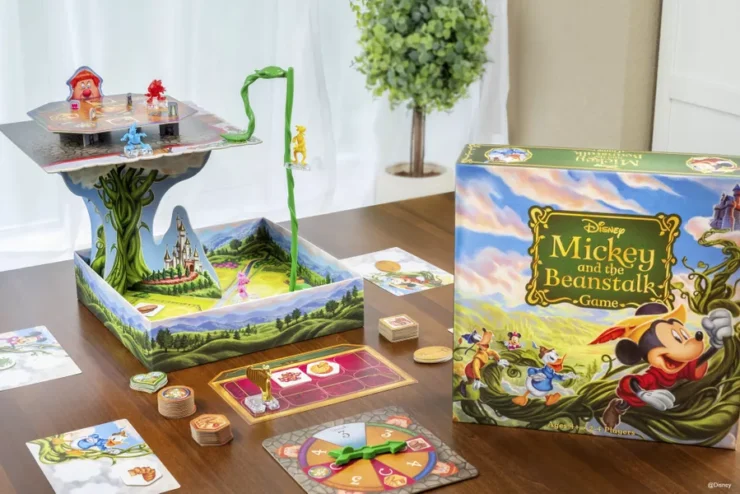 Colorful Disney board game "Mickey and the Beanstalk" displayed on a wooden table, featuring a 3D game board, character pieces, and game cards, set in a bright indoor environment with a plant in the background.