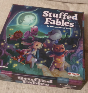 Colorful box cover of the board game "Stuffed Fables," featuring whimsical stuffed animal characters on an adventure under a moonlit sky, designed by Jerry Hawthorne and published by Plaid Hat Games.