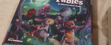 Colorful box cover of the board game "Stuffed Fables," featuring whimsical stuffed animal characters on an adventure under a moonlit sky, designed by Jerry Hawthorne and published by Plaid Hat Games.