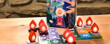 Tic Tac Trek travel game displayed on a wooden table, featuring a vibrant game box and unique game pieces shaped like flames and tokens. Ideal for two players, ages 8 and up, with a playtime of 15 minutes. Perfect for on-the-go family fun.