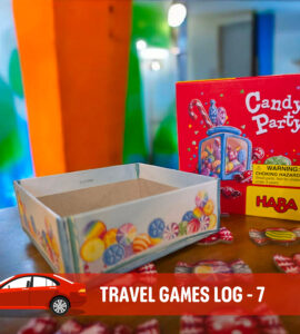Colorful Candy Party game box by HABA displayed on a table, featuring candy tokens scattered around, with a blank game container nearby. The background showcases vibrant painted walls, enhancing the playful atmosphere of family travel games.
