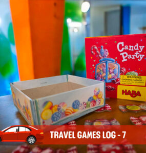 Colorful Candy Party game box by HABA displayed on a table, featuring candy tokens scattered around, with a blank game container nearby. The background showcases vibrant painted walls, enhancing the playful atmosphere of family travel games.