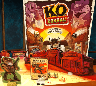 Colorful board game "K.O. Corral" displayed on a wooden table, featuring characters and a "Wanted" poster for Claude VonSnap, set in a Wild West theme with various game pieces and dice.
