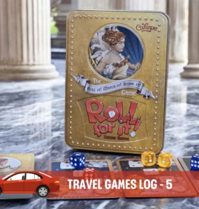 Alt text: A close-up of the board game "Roll for It!" Deluxe Edition displayed on a marble surface, featuring its distinctive gold tin box and colorful dice. Accompanying cards are spread out, showcasing artwork and game components, in a stylish setting with classical pillars in the background.