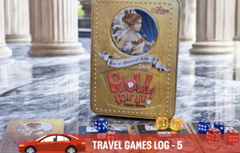 Alt text: A close-up of the board game "Roll for It!" Deluxe Edition displayed on a marble surface, featuring its distinctive gold tin box and colorful dice. Accompanying cards are spread out, showcasing artwork and game components, in a stylish setting with classical pillars in the background.