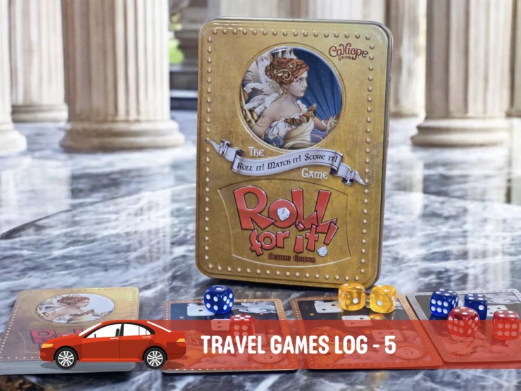 Alt text: A close-up of the board game "Roll for It!" Deluxe Edition displayed on a marble surface, featuring its distinctive gold tin box and colorful dice. Accompanying cards are spread out, showcasing artwork and game components, in a stylish setting with classical pillars in the background.