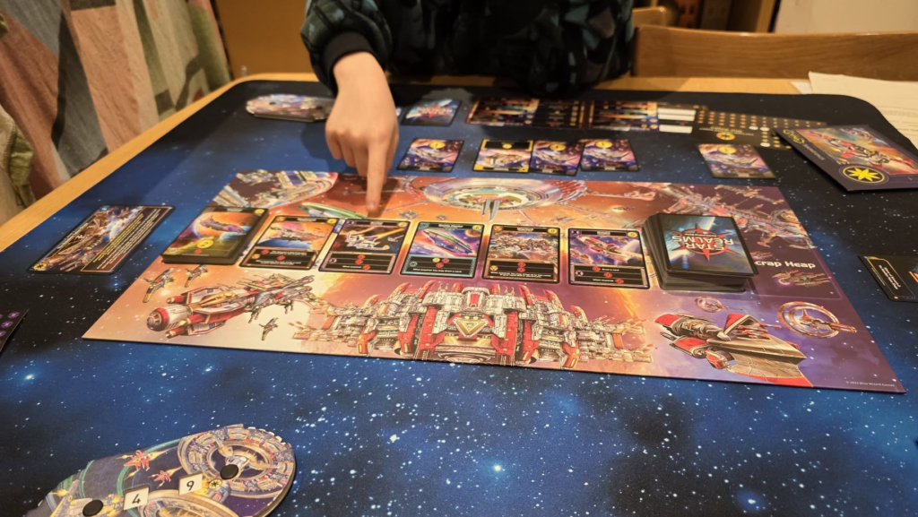 A person interacts with a vibrant space-themed tabletop board game on a blue starry mat, featuring colorful cards and game components, showcasing a strategic gameplay environment.