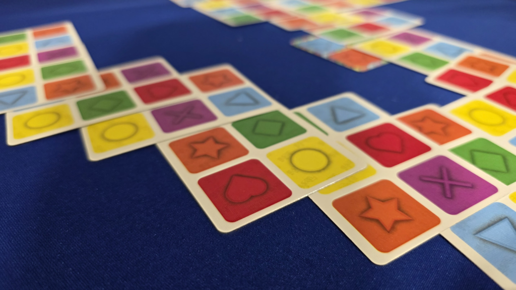 Colorful pattern-matching game cards featuring various shapes and colors arranged on a blue background, highlighting an engaging tabletop gaming experience.