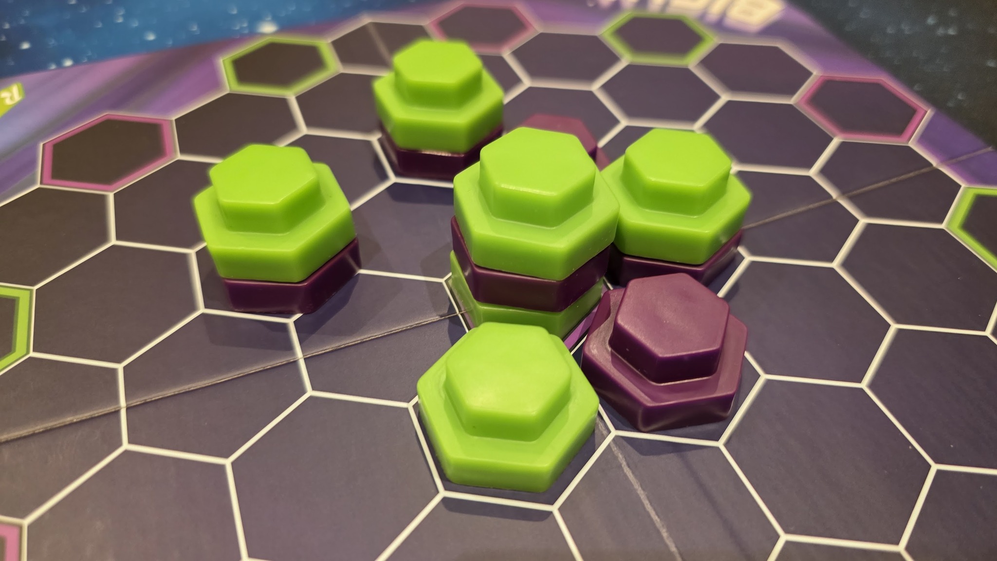 Image of a colorful board game setup featuring hexagonal game pieces in green and purple arranged on a hexagonal grid. The vibrant colors and unique shapes enhance the playful atmosphere of strategic gameplay.